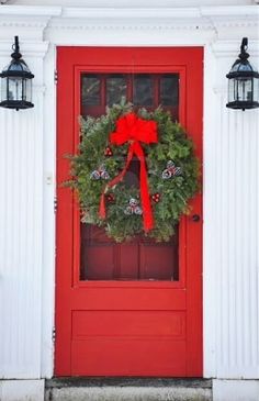 a red front door with a wreath on it and two lights hanging from the side