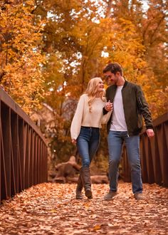 a man and woman walking across a bridge in the fall