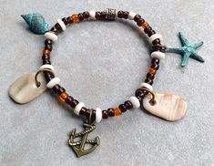 "Easy on and off bracelet has 2 hand picked sea shells I found on the beach at the Outer Banks of North Carolina. They are with a Green Patina Whelk Charm, a Green Patina Star Fish Charm, and a Brass Anchor Charm. Indonesian translucent Brown and Orange Beads and Luhuanus Shell Beads make up an interesting background for the sea shells and charms. A Brass Tube highlights the color of the Anchor Charm. The bracelet is strung on sturdy elastic for an easy to wear bracelet (\"roll\" it over your hand and not \"snap\" it on). It is 7 1/2\" long." Obx Bracelets, Brass Tube, Anchor Charm, Green Patina, Star Fish, Shell Beads, Outer Banks, Hand Picked, How To Make Beads