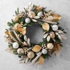 a christmas wreath with gold, silver and white ornaments hanging from the side on a wall