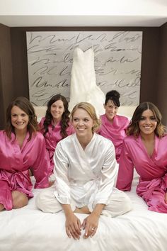 a group of women sitting on top of a bed wearing pink robes and smiling at the camera