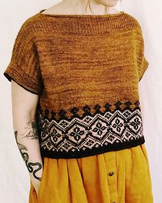 a woman with red hair wearing a brown sweater and yellow skirt standing in front of a white wall