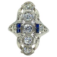 This is a fine antique Art Deco diamond and natural sapphire ring circa the 1920s. This stunning ring is comprised of 7 diamonds and 4 natural blue sapphires. Five old European cut diamonds are prong-set in octagonal settings down the length of the center and are flanked by four square natural blue sapphires, two per side. An additional round diamond is perched on each shoulder for a total of seven diamonds. Crisp filigree and milgrain detailing have stood the test of time. Diamonds approximatel Gold Stacking Rings Wedding, Gold Shield, Filigree Ring Gold, Diamond Cocktail Rings, White Gold Jewelry, Wedding Rings Vintage, Gold Filigree, European Cut Diamonds, Filigree Ring