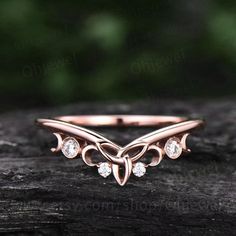 a rose gold ring with three diamonds on the side, sitting on top of a piece of wood