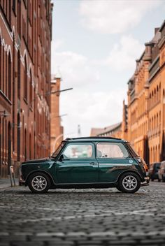 a small green car parked on the side of a road next to tall brick buildings