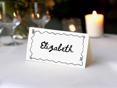 a place card sitting on top of a table next to some wine glasses and candles