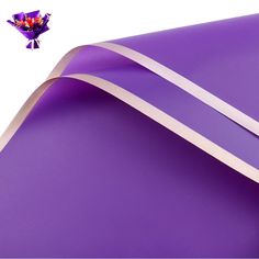 a roll of purple paper with white ribbon on it and a bouquet of flowers sticking out of the corner