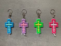 four different colored cross key chains on a gray surface, one is made out of plastic beads