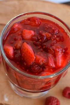 a glass filled with fruit on top of a cutting board next to raspberries