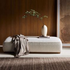 a white vase sitting on top of a bed next to a brown rug and wooden wall