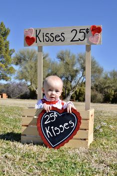 a baby sitting on top of a wooden crate holding a sign that says kisses 25 and kisses