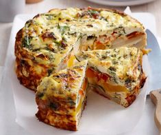 a cheese and vegetable quiche on a white plate with a knife next to it