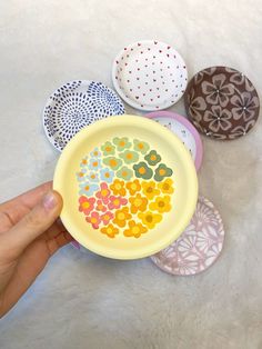 a hand holding a yellow bowl filled with colorful candies on top of a white surface