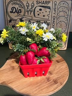 some strawberries and daisies in a red basket on a wooden table next to a sign