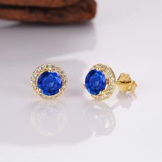 Add a little luxury, class, and sophistication to your look with our breathtaking Jia sapphire earrings. Made from our stunning gold on sterling silver materials, each iconic earring features a whopping 0.75-carat center sapphire. We’ve also added numerous stunning CZ crystals around the outer rim of the earrings for an unrivaled shine. ✦ DETAILS ✦ ✧ Handcrafted ✧ .75 Carat center stone ✧ Sapphire and cz crystals ✧ 8mm (about 6/8 inch round) ✧ Sterling Silver 925 or 14K Rose Gold Vermeil or 14K Elegant Yellow Gold Jewelry With Lab-created Sapphire, Sapphire Birthstone Earrings In Fine Jewelry, Sapphire Earrings With Halo Setting For Gift, Sapphire Earrings With Halo Setting As Gift, Sapphire Earrings With Halo Setting For Anniversary, Sapphire Birthstone Earrings Fine Jewelry, Sapphire Birthstone Earrings For Formal Occasions, Luxury Sapphire Cubic Zirconia Earrings, Sapphire Round Cut Earrings For Anniversary