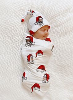 a baby wrapped up in a santa hat sleeping on top of a white bed sheet