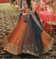 a woman in an orange and blue lehenga is posing for the camera with her hand on her hip