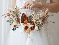 a woman in white dress holding a bouquet with feathers and flowers on it's side