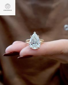 a close up of a person's hand holding a ring with a pear shaped diamond