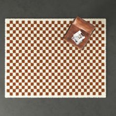 a brown and white checkered rug with a leather bag sitting on top of it