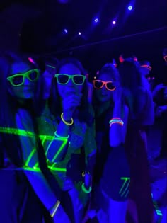 three young women wearing neon glasses in the dark at a club or nightclub with their arms around each other