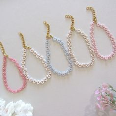 four necklaces with pearls and gold chains on a white table next to pink flowers