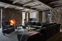 a living room filled with furniture and a fire place next to a stone wall covered in logs