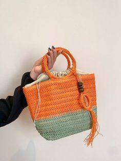 a woman is holding up a crocheted orange and green handbag with tassels