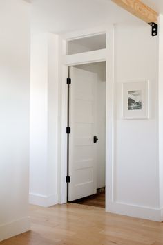 an open door in a white room with wood flooring and framed pictures on the wall