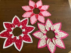 three paper flowers sitting on top of a wooden table next to each other, one pink and the other red