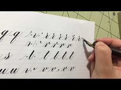 a person writing with a pen on top of a piece of paper that has cursive writing on it