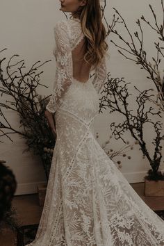 a woman in a white wedding dress standing next to some branches and flowers with her back turned