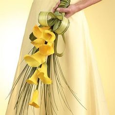 a woman in a white dress holding a bouquet of yellow calla lilies and pine needles