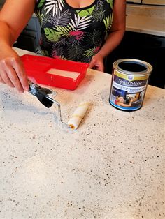 a woman is painting the counter top with white paint and a red container on it