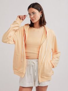 a young woman wearing glasses and an orange top is standing in front of a white background