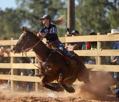 a woman riding on the back of a brown horse in front of a wooden fence