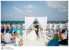 a couple getting married on the beach by their wedding party and guests watching them walk down the aisle