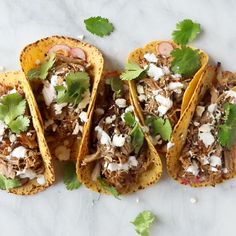 three tacos with meat, cheese and cilantro on a white tablecloth