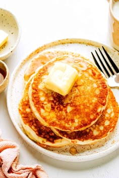 pancakes with butter and syrup are on a plate next to a fork, knife and cup