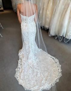 a woman in a wedding dress is looking at her veil on the floor next to some dresses