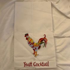 a white towel with a colorful rooster on it's side and the words fruit cocktail written in red