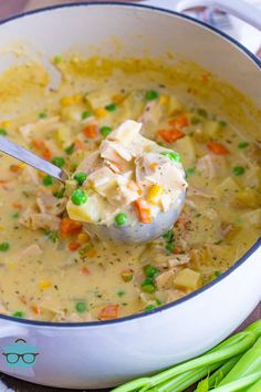 a ladle full of soup with peas and carrots on the side next to celery