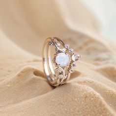 a white opal and diamond ring sitting on top of sandy ground with sand in the background