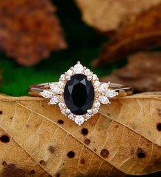 a black and white diamond ring sitting on top of a leaf covered ground with leaves in the background