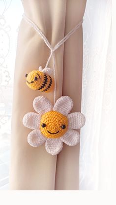 two crocheted bees hanging from a white curtain with a flower attached to it