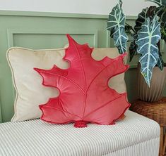 a red leaf pillow sitting on top of a white bench next to a potted plant