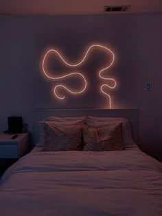 a bed with white sheets and pillows in front of a neon sign on the wall