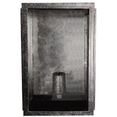 a black and white photo of a silver vase in a glass case on the wall