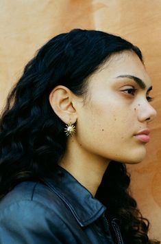 a woman with long black hair is wearing a leather jacket and has earrings on her ear