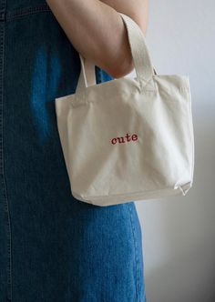 a woman is holding a white bag with the word cutie on it, in red